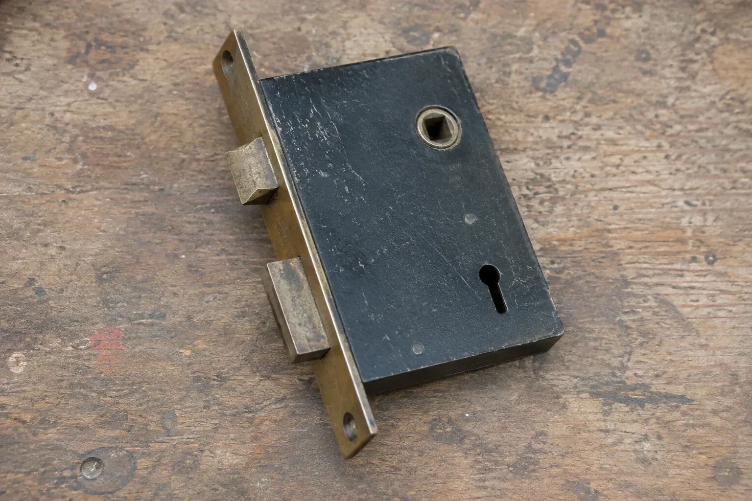 Closed mortise lock case with spindle opening, keyhole, latch and deadbolt on a wooden workbench. — Vintage Mortise Lock Service, Whitchurch-Stouffville