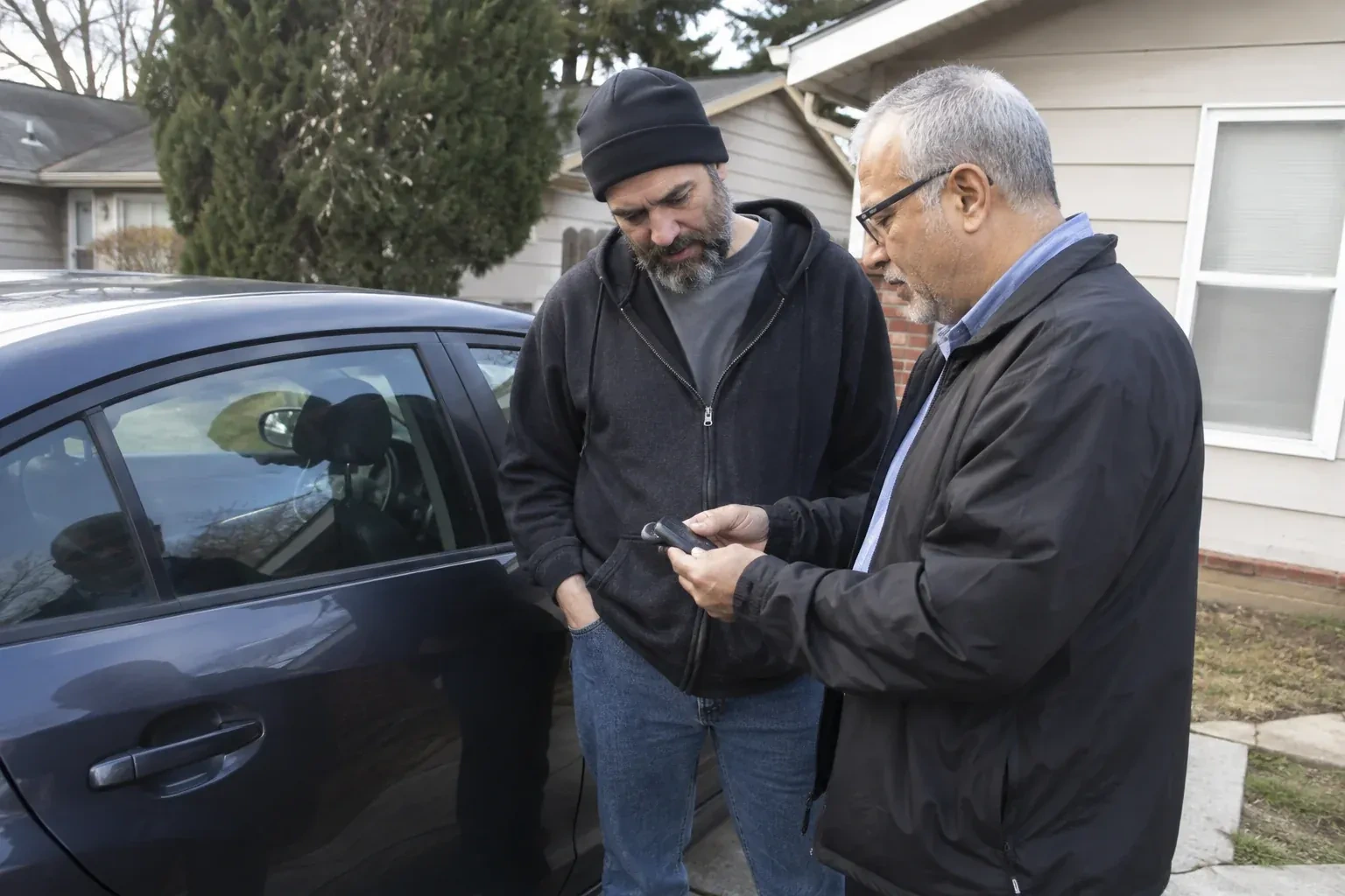 Two adults discussing a key fob beside a parked car. — Car Lockout Service, Whitchurch-Stouffville